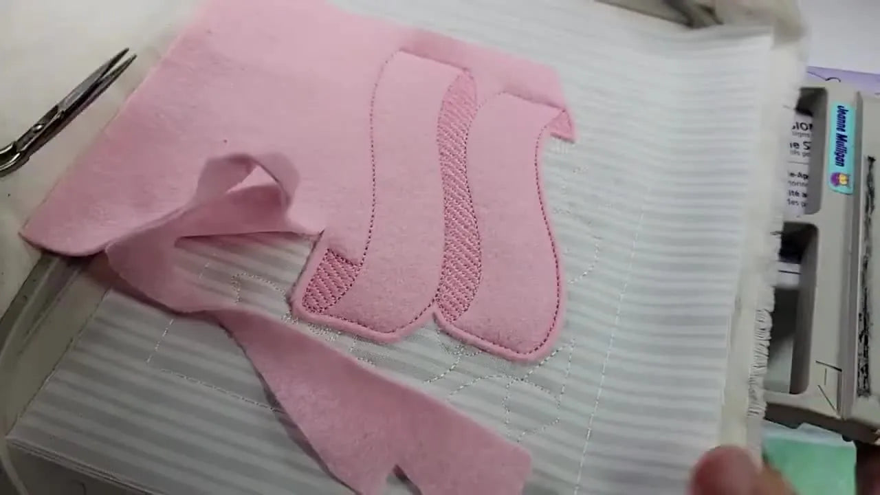 Close-up of the Baby Lock Luminaire 2 stitching black lettering onto a pink felt banner inside the hoop.