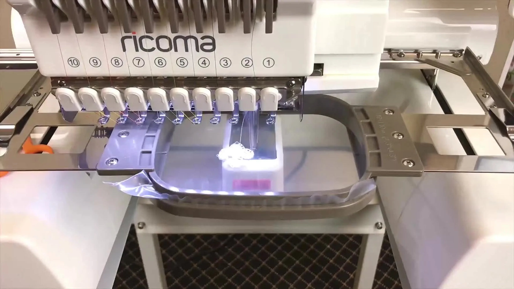 A close-up of the embroidery machine stitching a white freestanding lace design onto clear water-soluble stabilizer in a tubular hoop.