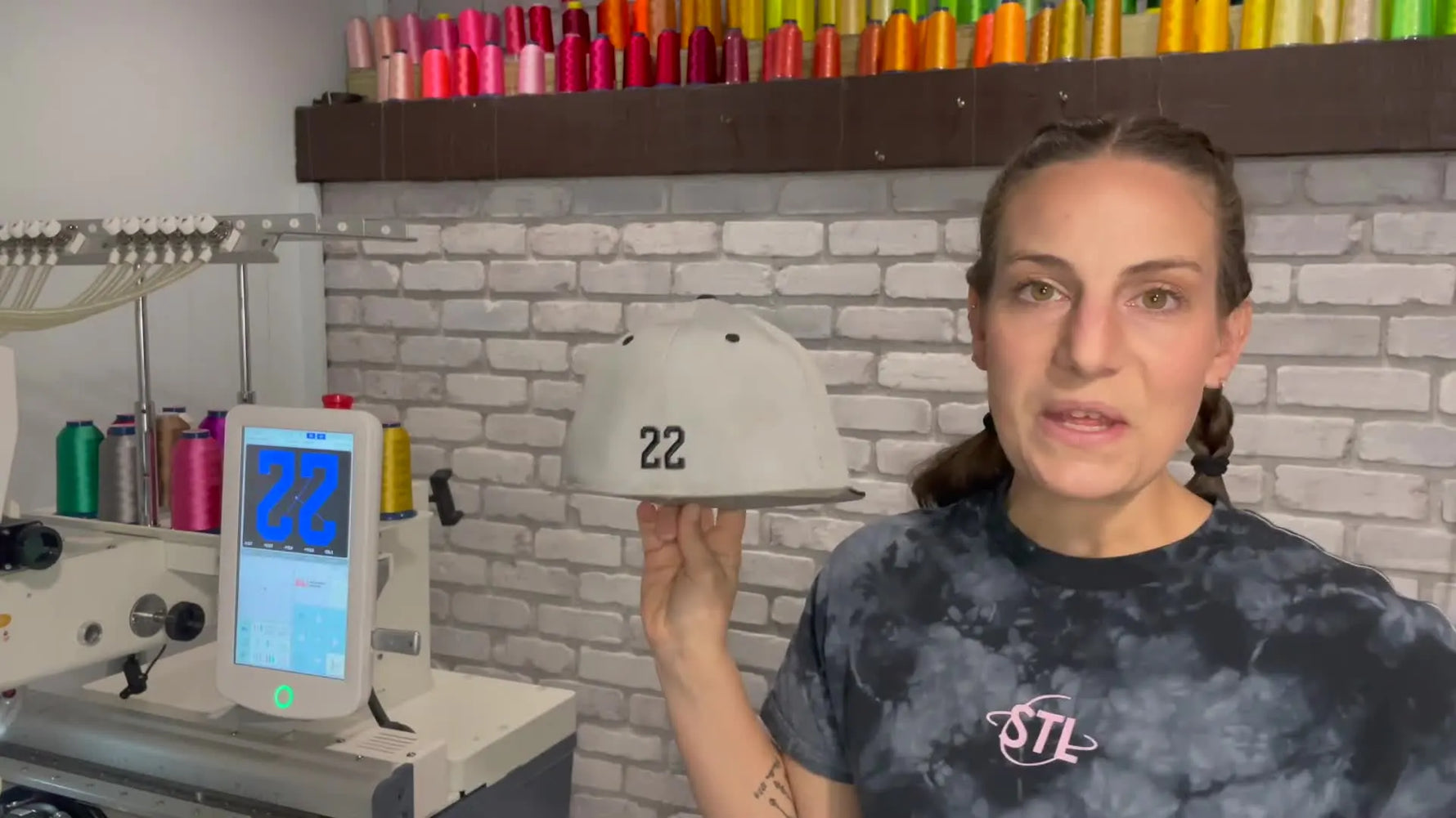 A finished grey baseball cap is held up to show a clean, centered “22” stitched on the back panel.