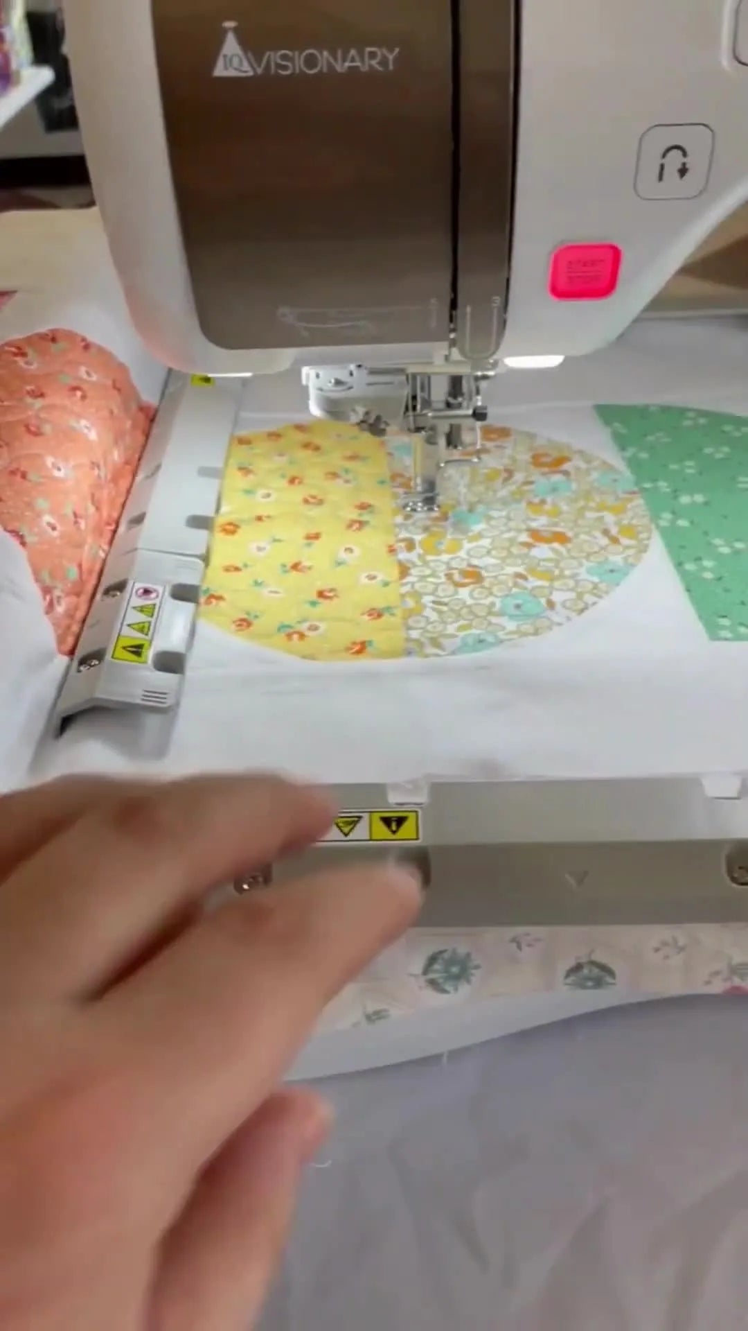 A close-up of a hand adjusting a rectangular magnetic hoop on a quilt sandwich, with the magnets clearly visible.