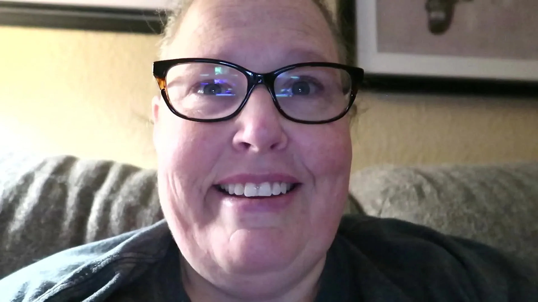 Woman smiling at the camera, wearing glasses and a grey t-shirt.