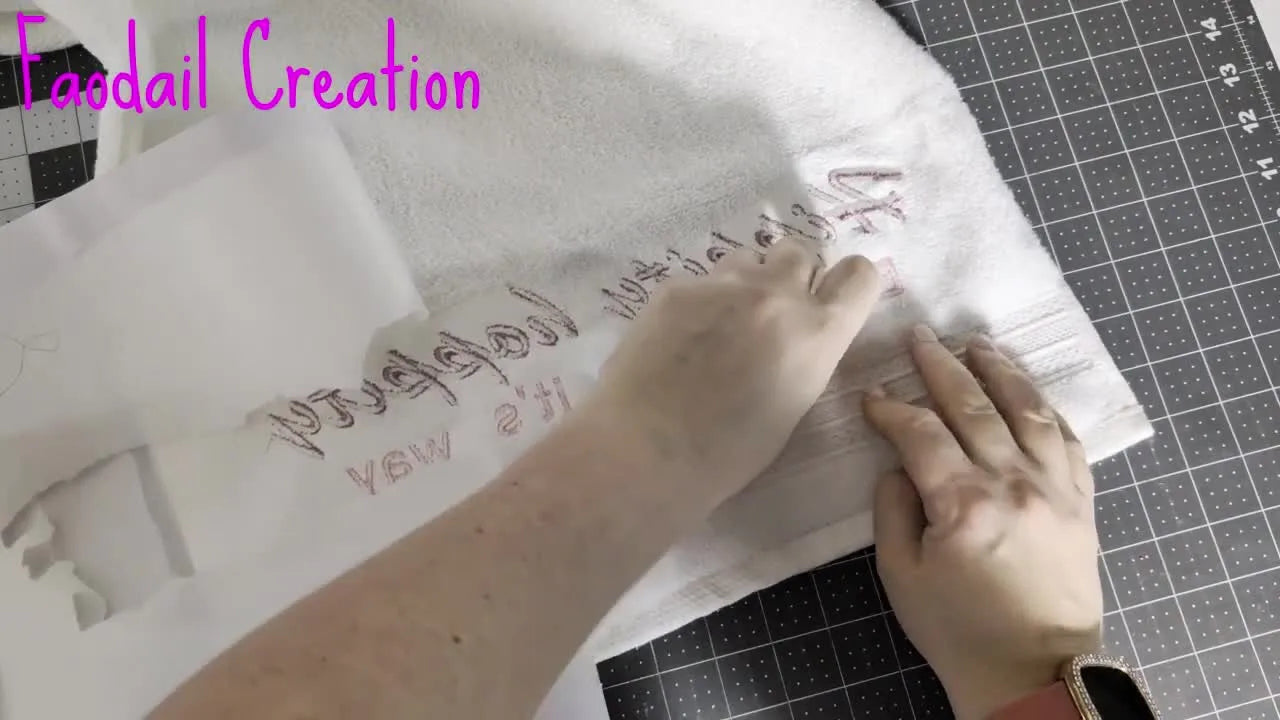 A finished white terry hand towel hangs on a rack with crisp pink “Hippity hoppity” embroidery centered neatly above the decorative band.