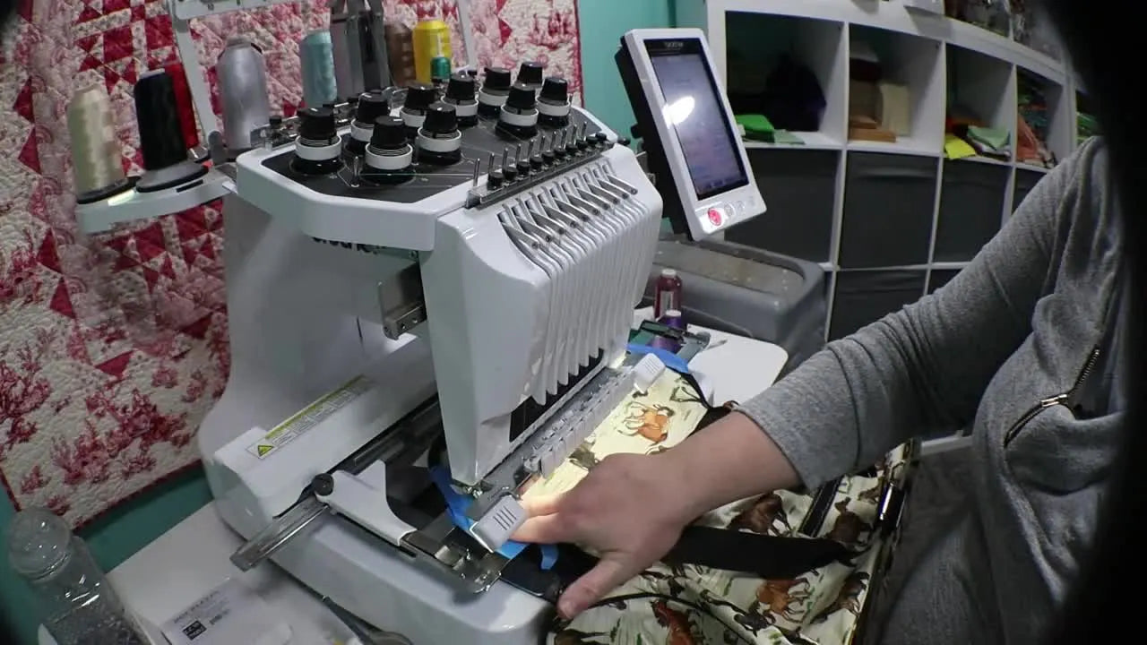 Close-up of the Brother PR1000e stitching a name while the heavy duffel bag is supported to prevent drag.