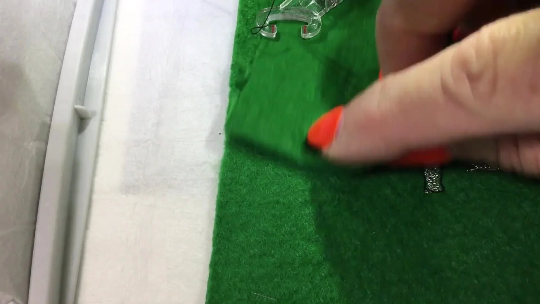 A hand folds the top section of green felt down over a stitched monogram while the piece is still in the hoop, forming the in-the-hoop pocket.