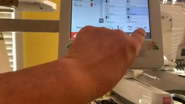 Close-up of a Brother multi-needle machine stitching a shiny gold letter onto a thick woven vinyl placemat inside a magnetic hoop.