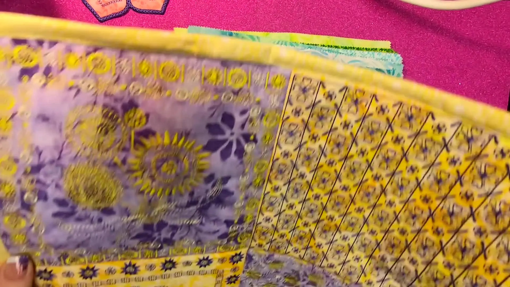 An overhead reveal of the finished yellow-and-purple “China Tropical” wall hanging showing how a single layer cake palette can drive both fabric and thread choices.