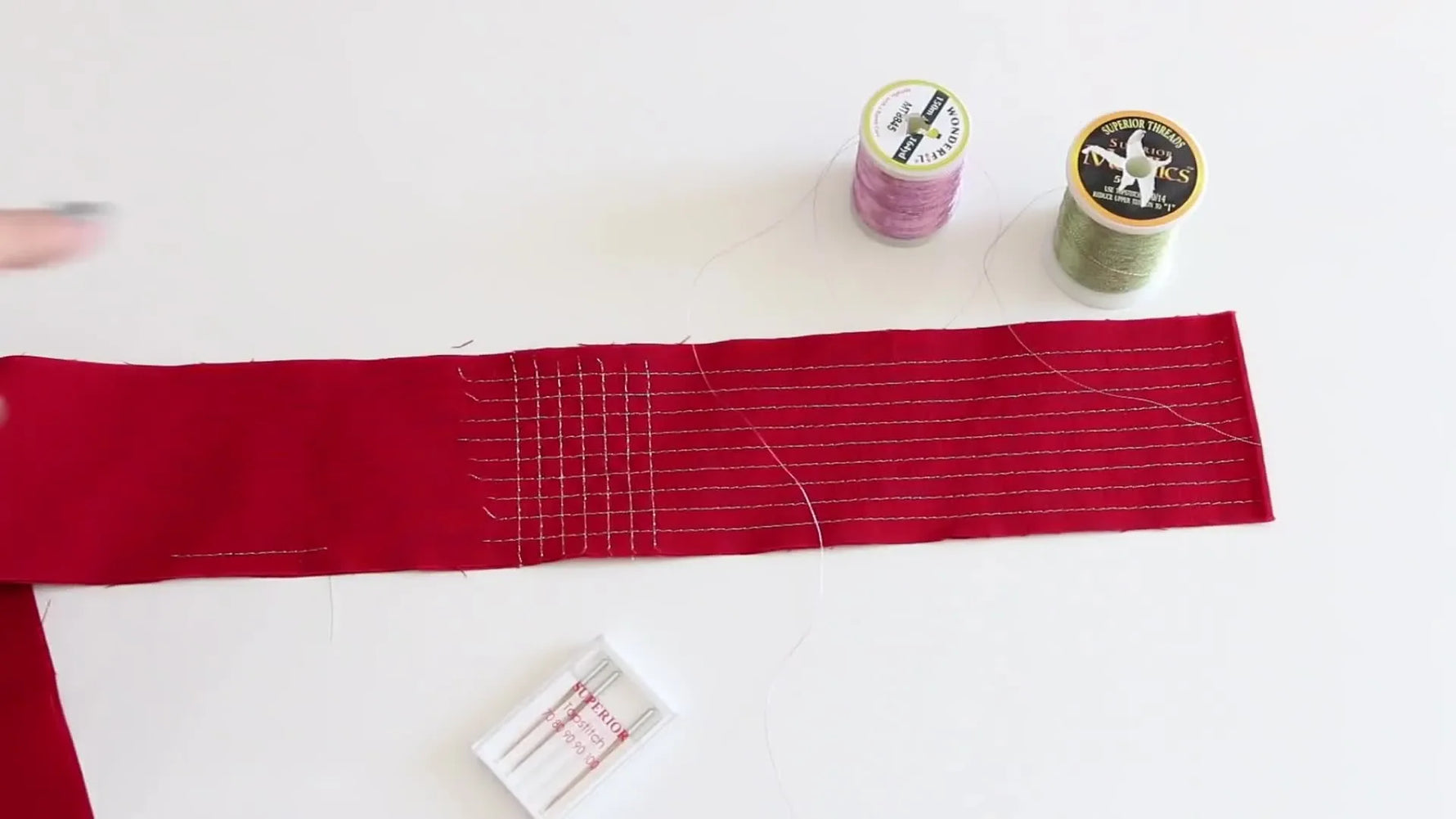 Hand pointing at red fabric with sample metallic thread stitching.