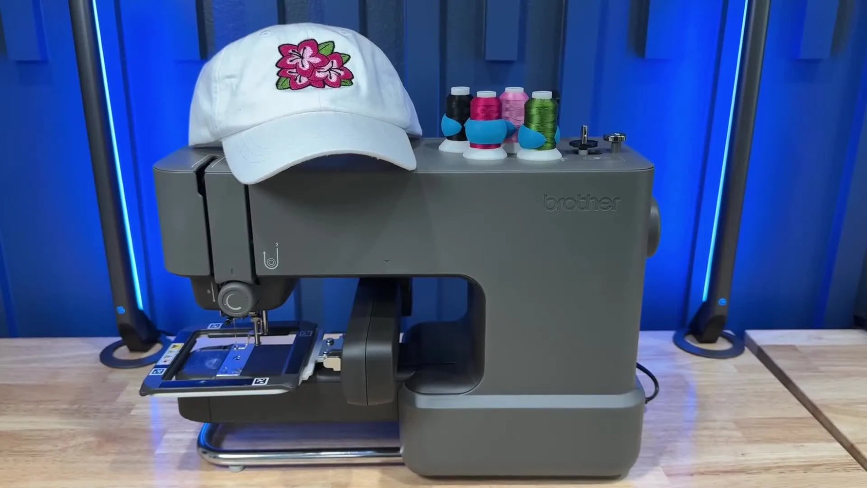 A Brother Skitch PP1 sits behind a finished embroidered baseball cap, with thread spools nearby—showing the end goal before you start.