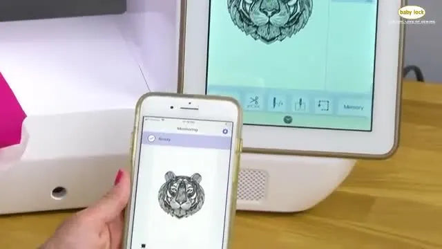 A split view shows the tiger embroidery design mirrored instantly from the Baby Lock Solaris screen to the IQ Intuition Monitoring app on an iPhone.