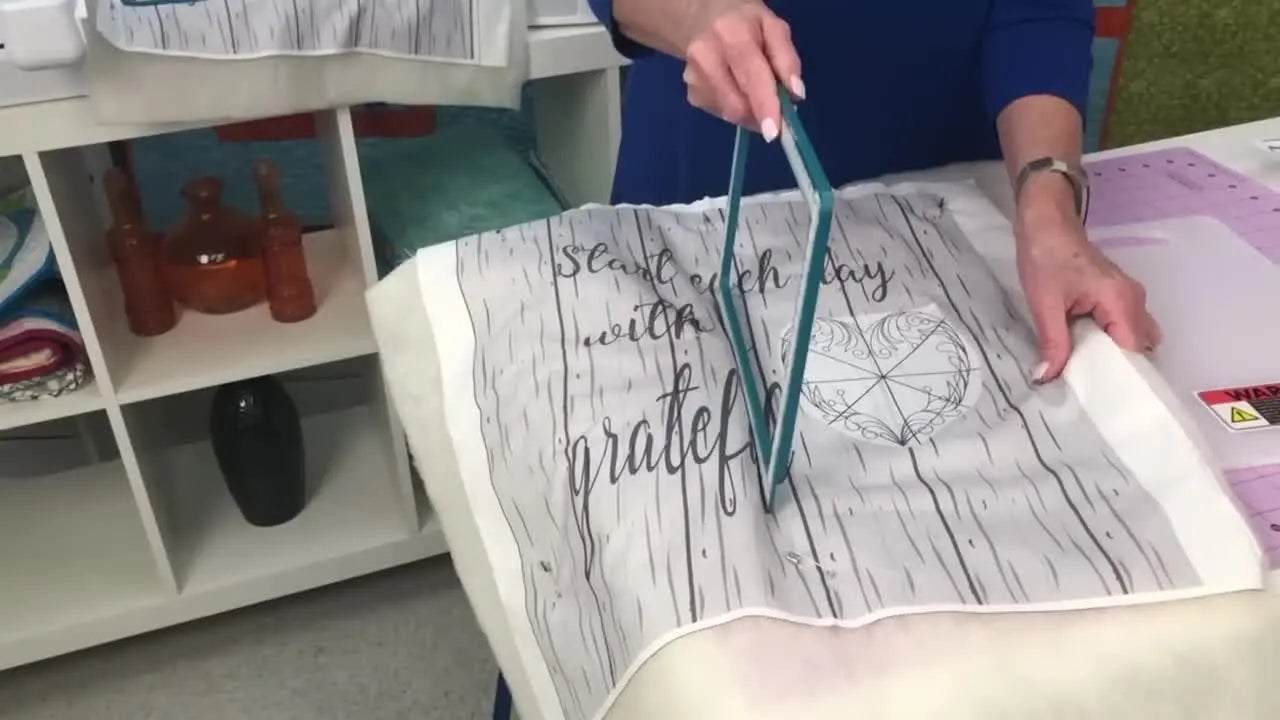 A close-up of the magnetic top frame being dropped onto fabric, locking the project flat and secure in the hoop.