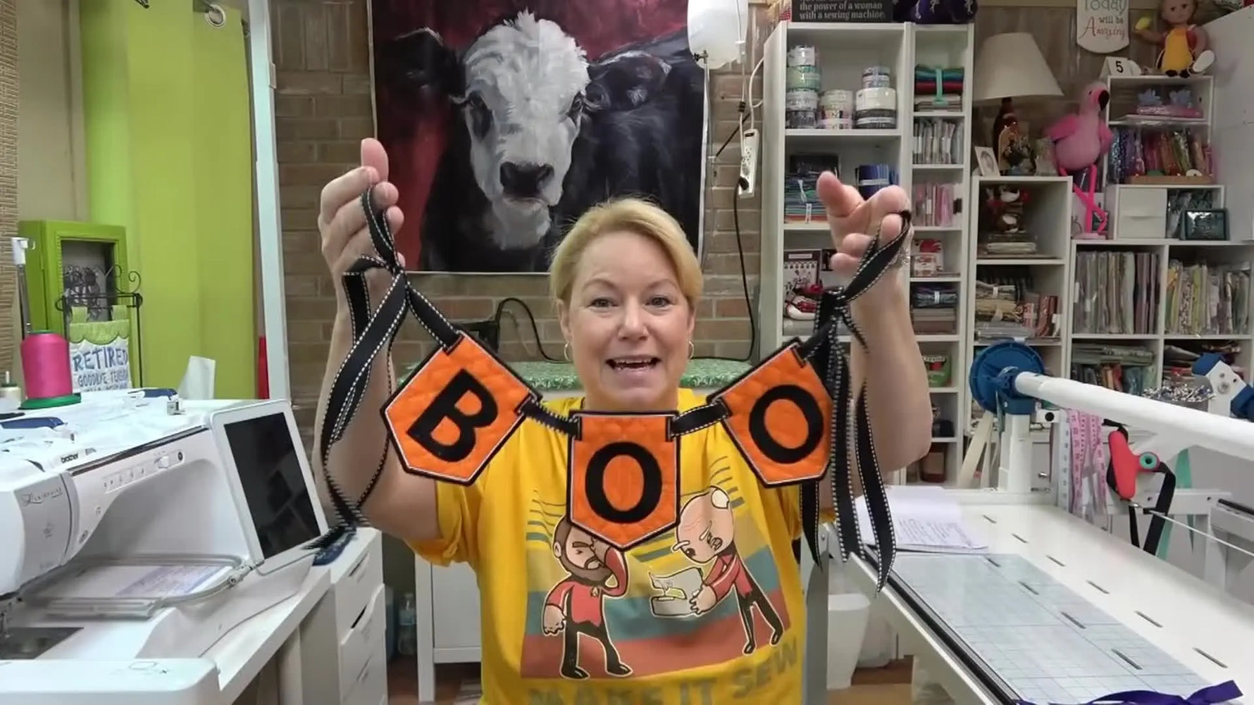 A finished “BOO” bunting banner is held up to show crisp satin borders, clean lettering, and ribbon-ready pennants.