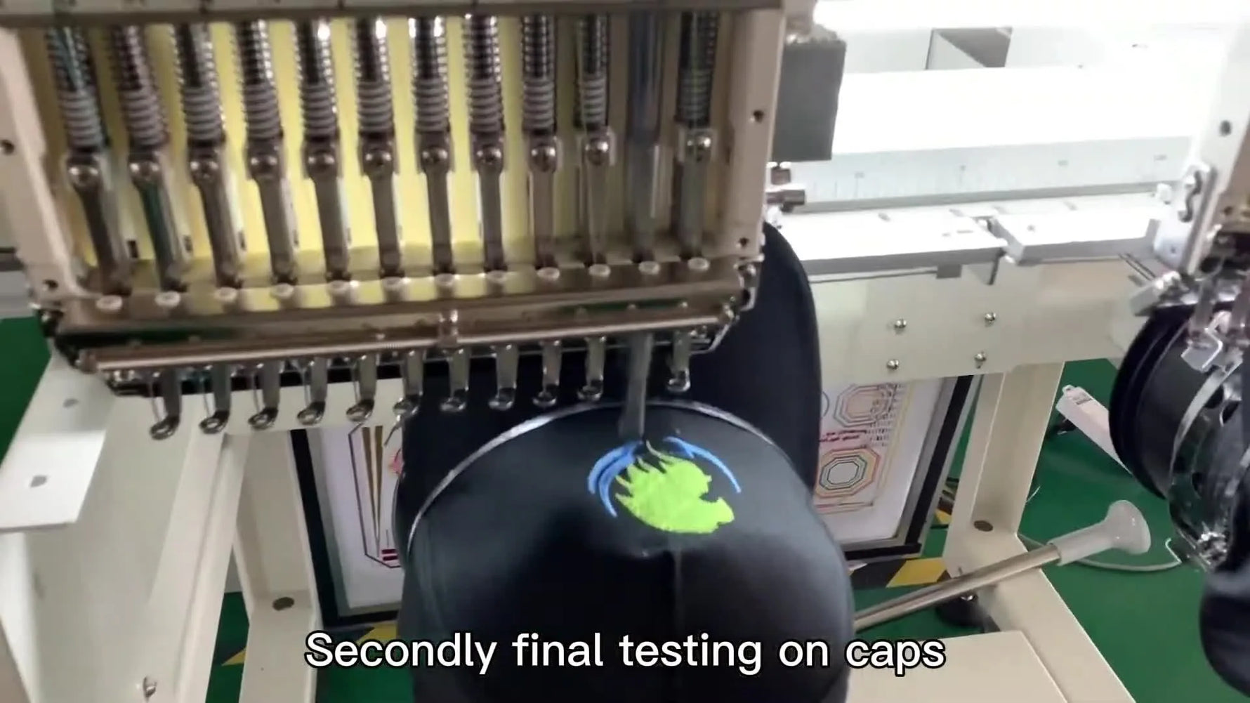Close-up of the needle stitching a green logo onto a black baseball cap during the final cap-driver test.
