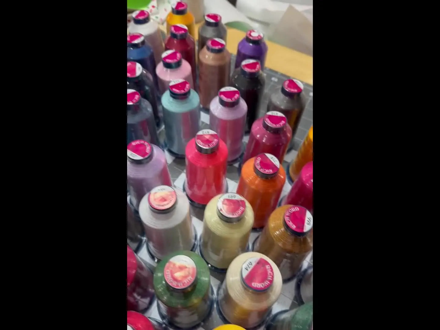 A wide tabletop reveal of 100 Rich Word polyester thread cones arranged in a color gradient for quick visual inventory.