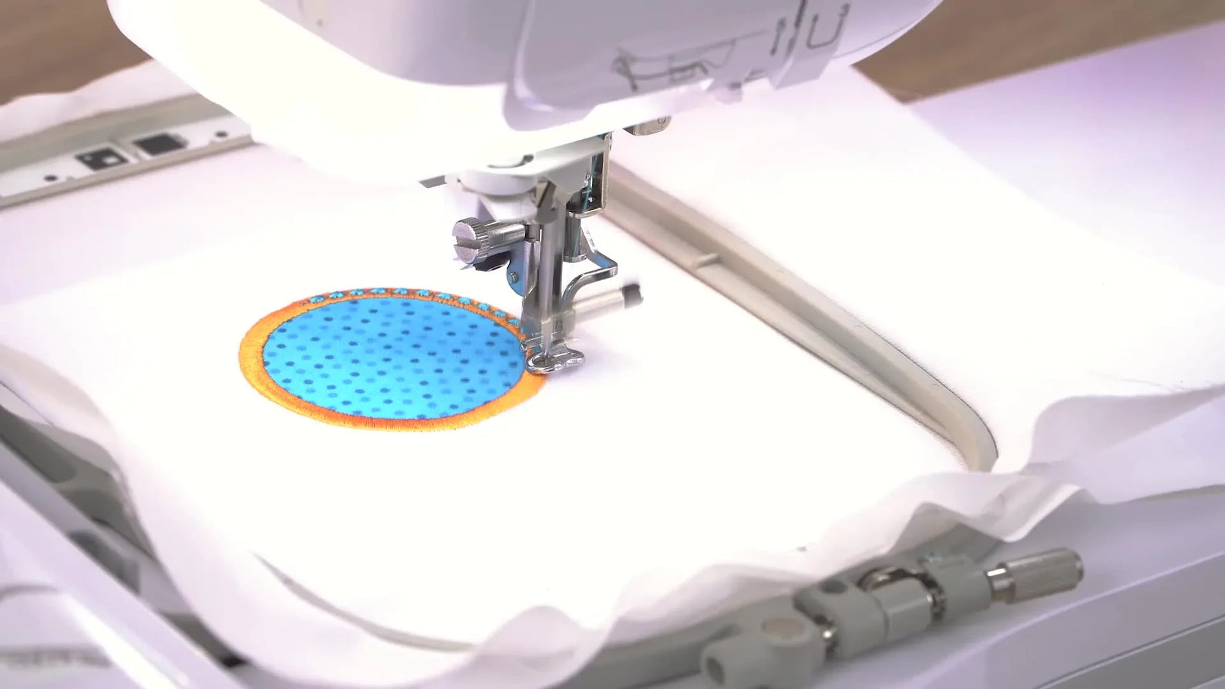 Close-up of the Brother Stellaire stitching the final blue candlewicking details over a wide orange satin border on a circle appliqué.