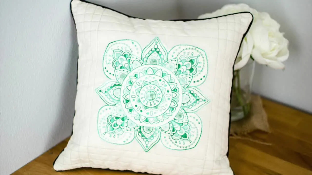 A close-up of the finished quilted pillow showing a detailed green mandala embroidery stitched with variegated thread.