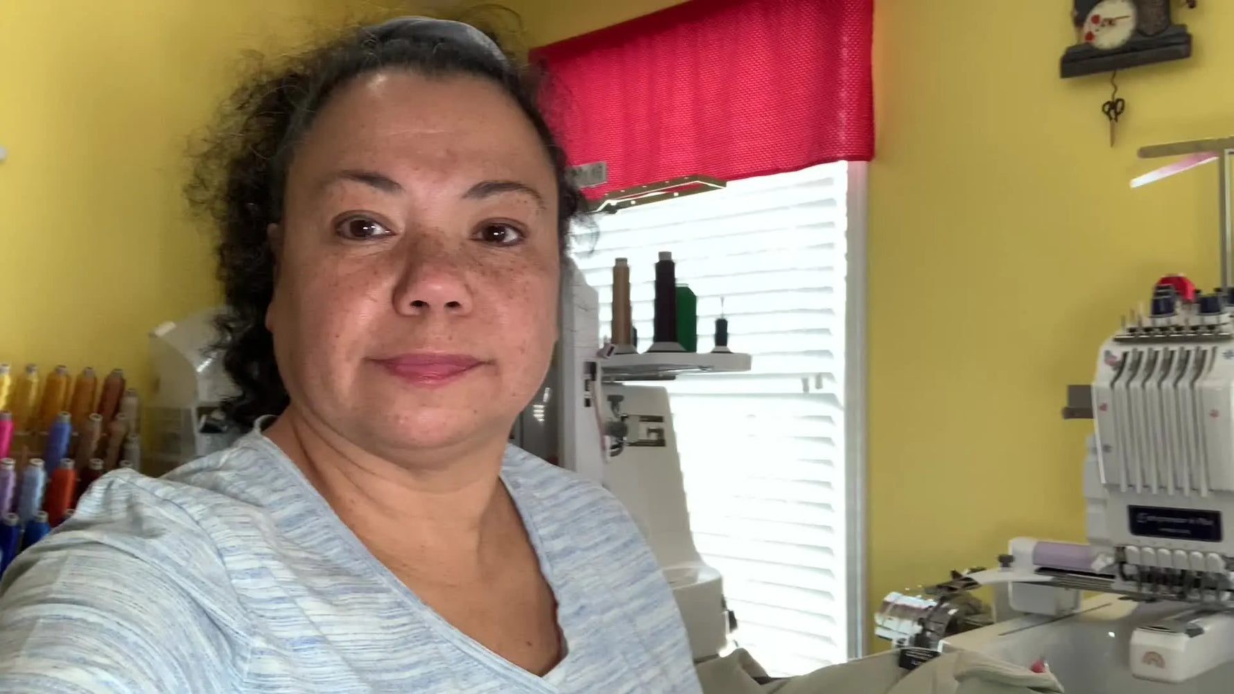 Woman smiling in front of embroidery machines, holding up a shirt.