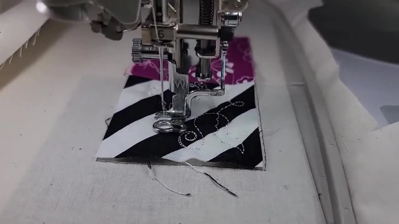 A close-up of the embroidery machine stitching a white witch quilting motif onto a striped fabric section in-the-hoop.