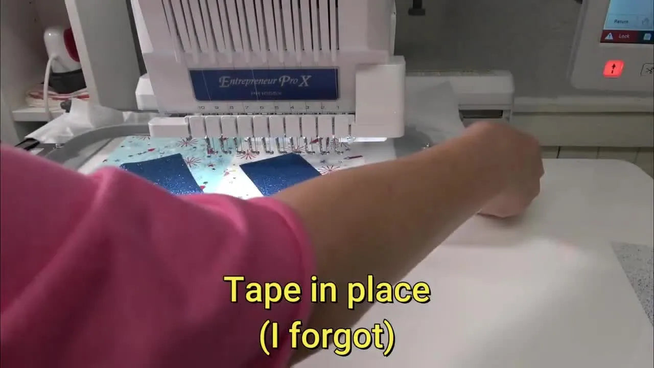 Hands place blue glitter vinyl onto the hooped area right before tackdown stitching, showing the exact moment vinyl can shift if it isn’t secured.