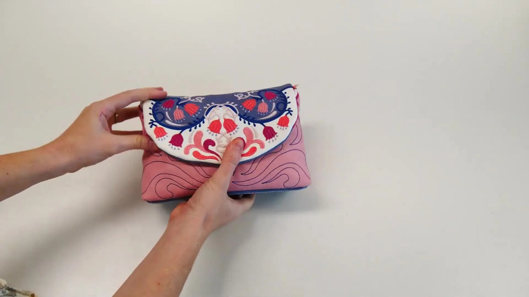 A finished pink-and-blue embroidered cosmetic bag is held up close, showing the wrap and clean boxed shape.