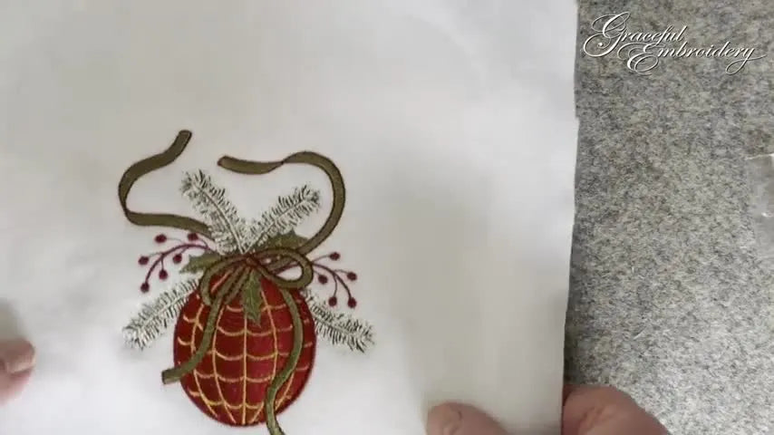 A close-up of a stitched Christmas bauble embroidery with ribbon and metallic details, ready to be mounted into a festive aperture card.