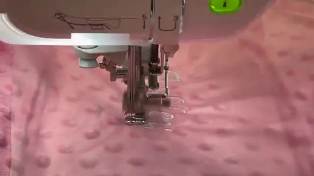 Close-up of a Janome embroidery machine stitching a name onto dimple dot minky with a clear water-soluble topper in place.