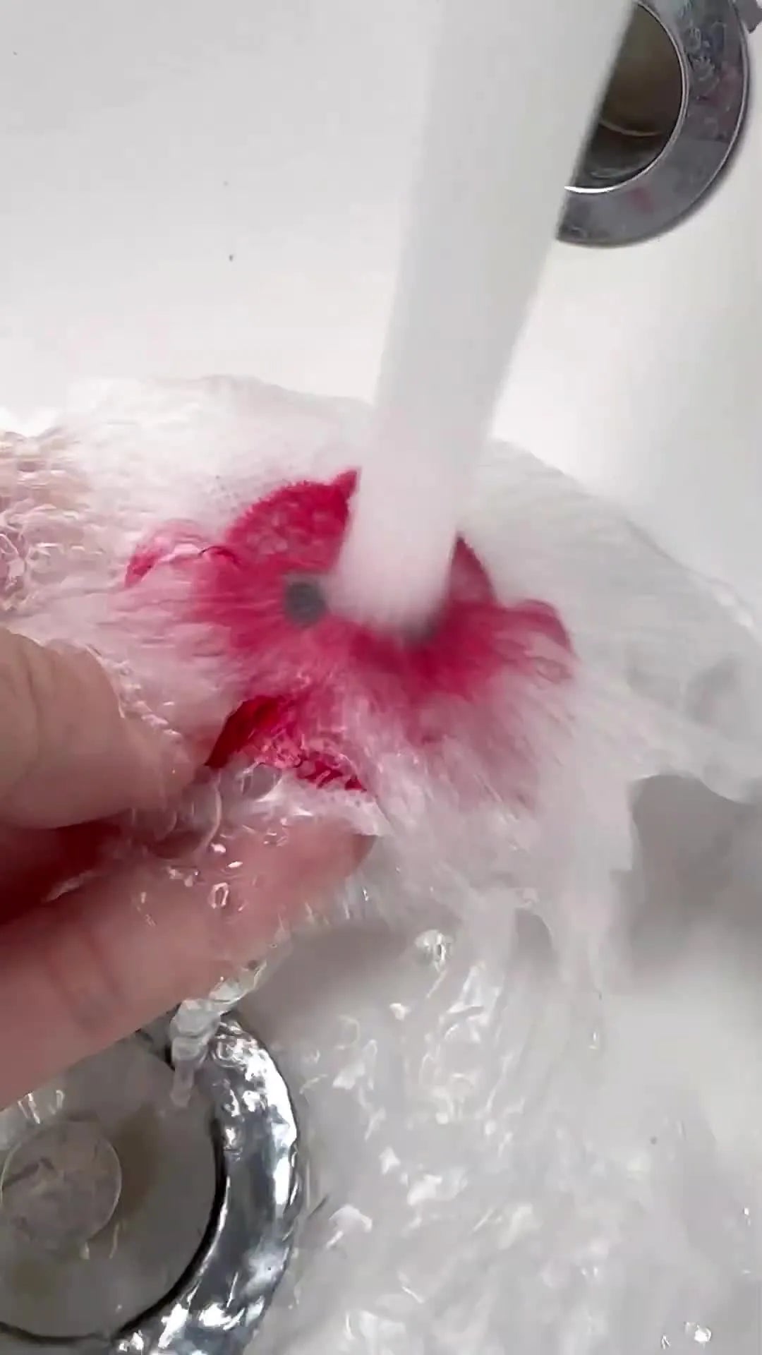 A crab patch is held under running water as the white water-soluble stabilizer dissolves and the red fringe blooms into a fluffy 3D texture.