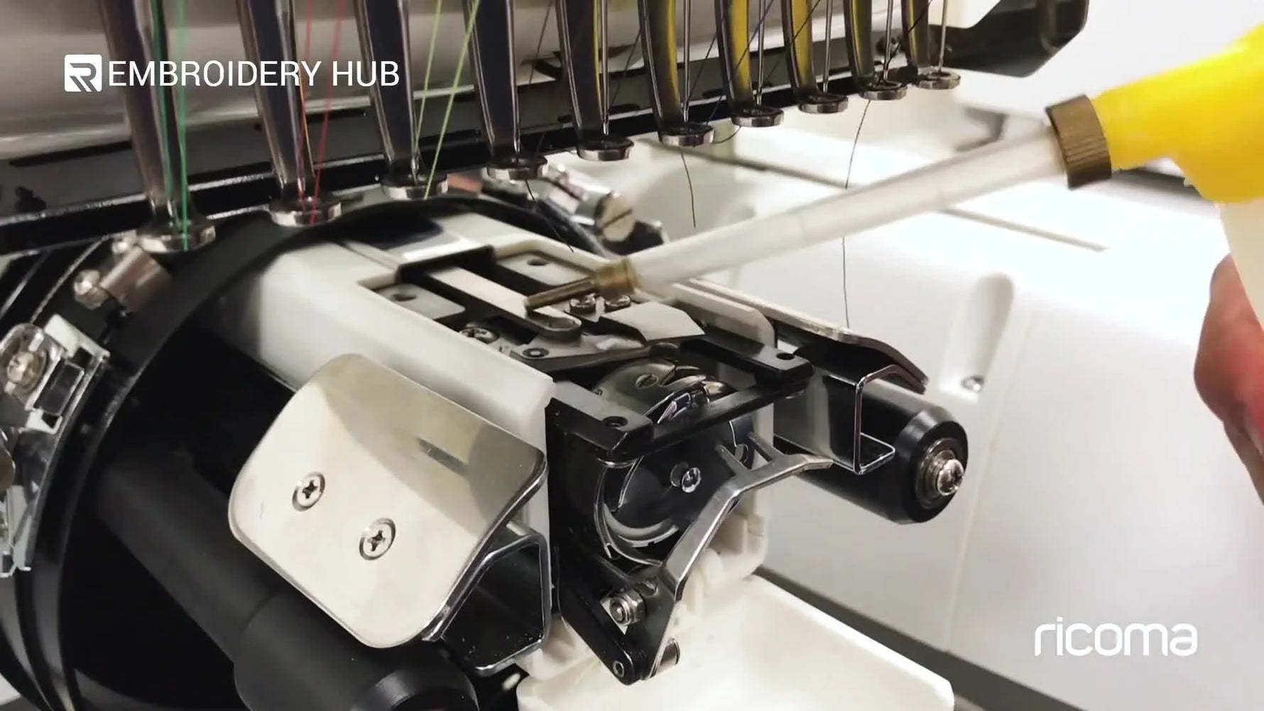 A close-up of sewing machine oil being applied to the reciprocating rod under the Ricoma EM-1010 needle plate.