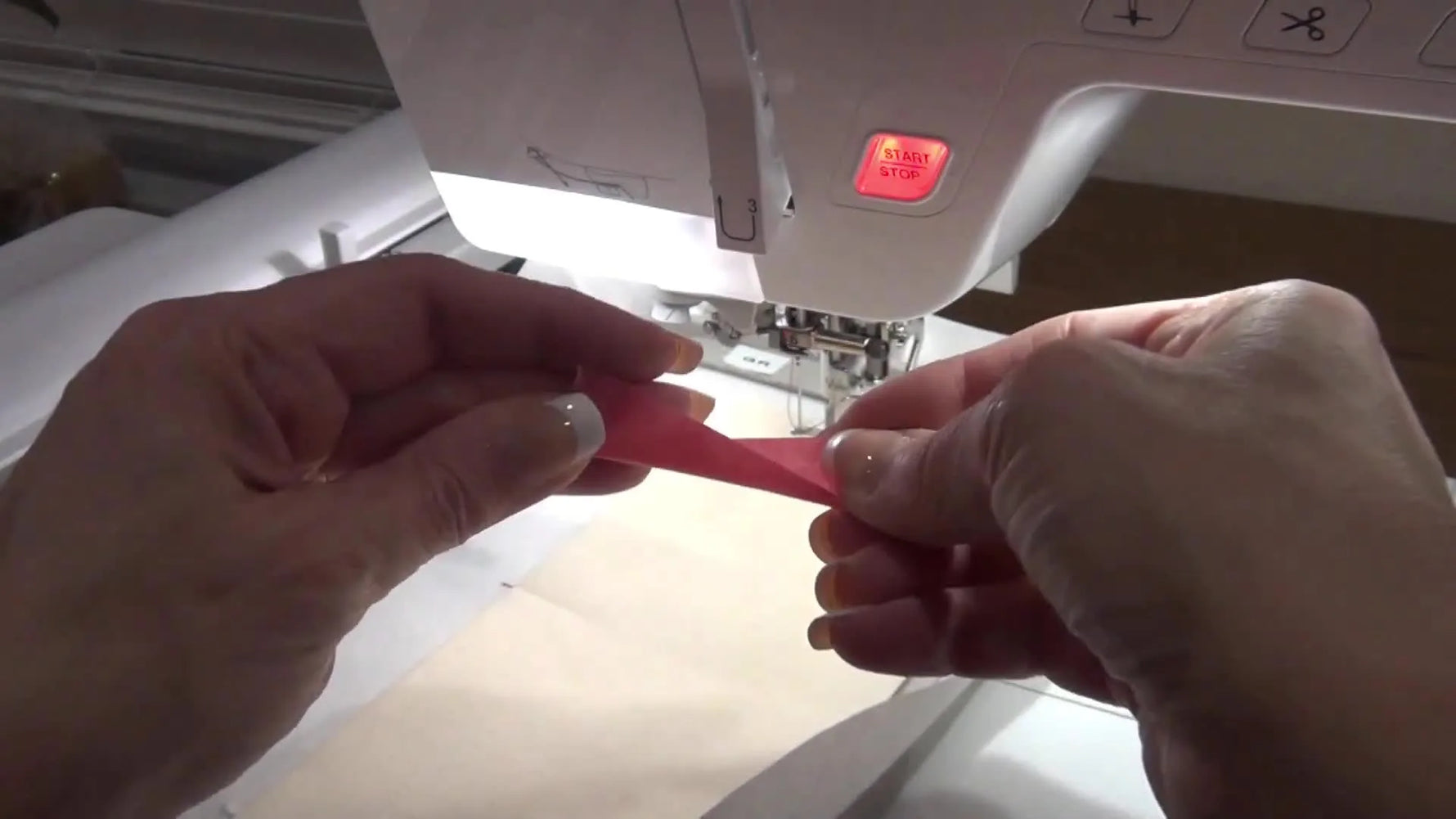 Pink embroidery tape securing the edges of the cream fabric to the stabilizer inside the hoop.